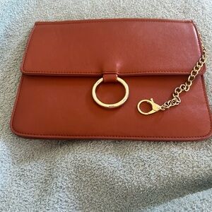 Brown leather like clutch with snap closure and gold tone hardware.  7.5” x 10”
